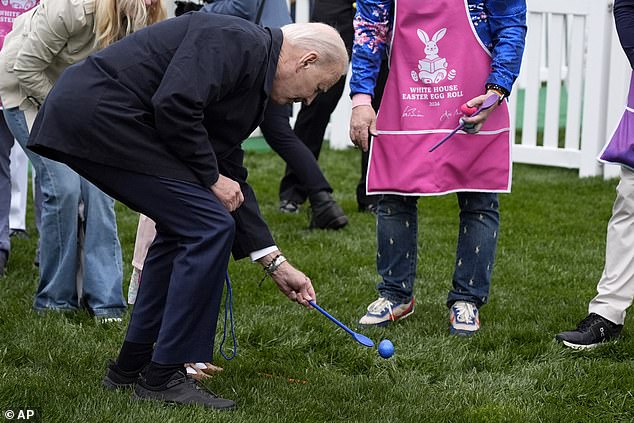 President Joe Biden holds a young person and rolls an egg