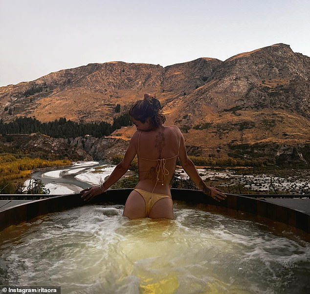 Taking to Instagram on Saturday, Rita showed off her enviable figure in a yellow bikini as she lounged in a hot tub while on a scenic mountain getaway with her sister Elena.