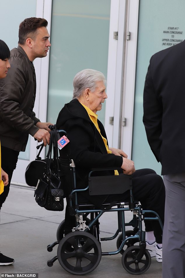 He supported his team in a yellow polo shirt, but he also wore a black fleece jacket, black sweatpants and black and white Nikes.  A man pushed Wilson's wheelchair while a woman placed a hand on his shoulder as they walked to a door to enter the arena