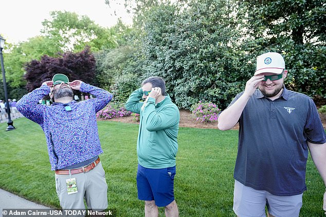 Friends try on eclipse glasses during a practice round for the Masters tournament