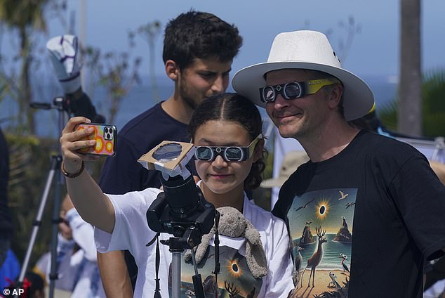 People take selfies while watching and photographing a total solar eclipse in Mazatlan, Mexico, Monday, April 8, 2024. They put a filter on their camera that points at the sky.