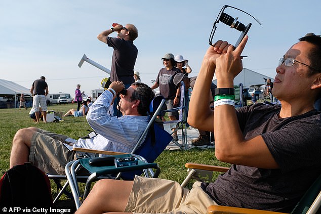 Amos Yew (R) uses a lens on an iPhone with protective sunglasses over the lens to record video of the early stages of the total solar eclipse on August 21, 2017 in Madras, Oregon.