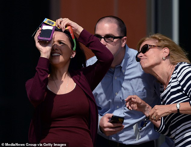 Kayla Ketz, left, uses eclipse glasses to photograph the solar eclipse with a smartphone as colleagues Joe Belovich and Nancy Dyer watch in Boston's Seaport District on Monday, August 21, 2017.