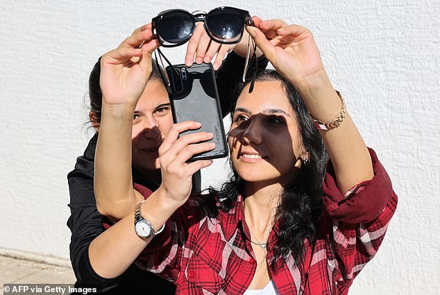 Women wearing sunglasses watch a partial solar eclipse via a smartphone camera in Ankara, on October 25, 2022.