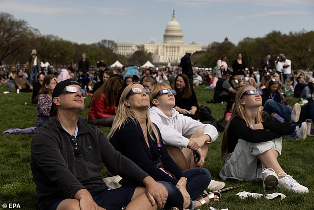 People on the National Mall watch a partial solar eclipse, with the US Capitol Building in Washington, DC, USA behind it.  The narrow path of totality crossed thirteen American states