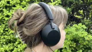 Someone wearing Sony WH-1000XM5 headphones against a green background