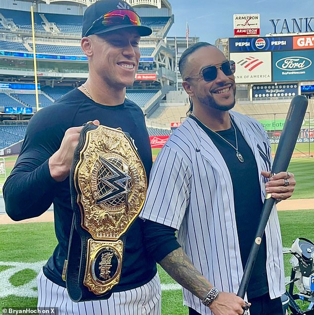 Judge and priest pose for photos together with a bat and the title at Yankee Stadium