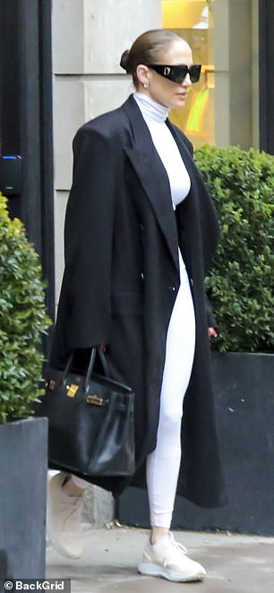 She also wore a white turtleneck crop top with matching leggings and sneakers under a black double-breasted maxi coat with huge shoulder pads.