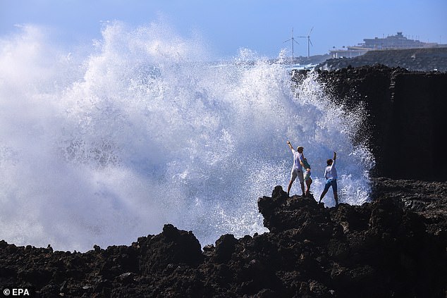 Tourists pose for photos on Wednesday as high waves break on the coast of La Palma, Gran Canaria, Spain