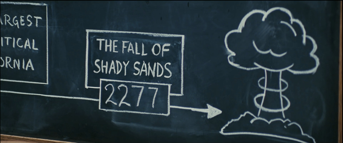 A screenshot from Fallout season 1, of a chalkboard drawing that reads “The Fall of Shady Sands: 2277” with an arrow pointing to a drawing of an atomic bomb explosion