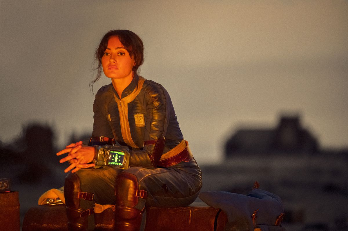 Lucy (Ella Purnell) sits by a fire, looking solemn in a still from Fallout