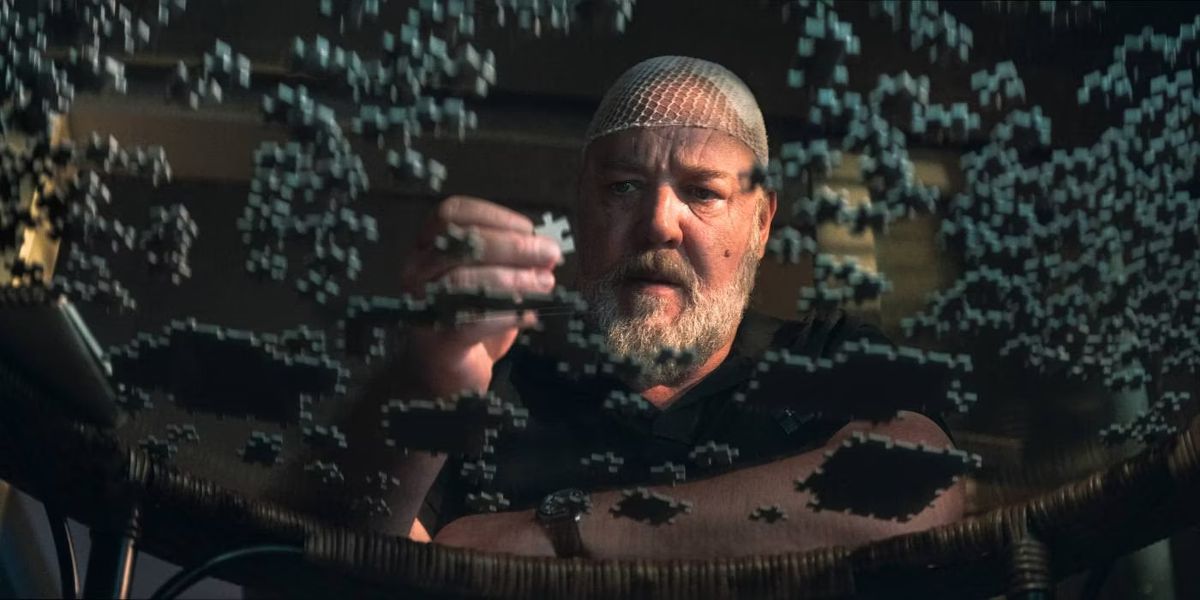 A man wearing a hairnet holds a puzzle piece and stares at a glass table full of puzzle pieces.