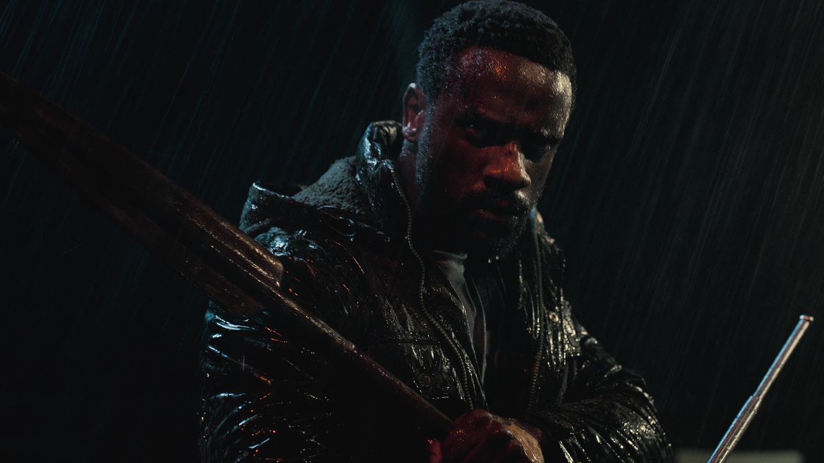 A man in a leather jacket standing in the rain and holding weapons.