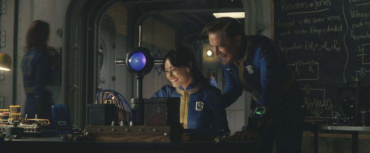 Lucy (Ella Purnell) and her father, Overseer Hank (Kyle Maclachlan) laugh about a science experiment in a still from Fallout season 1