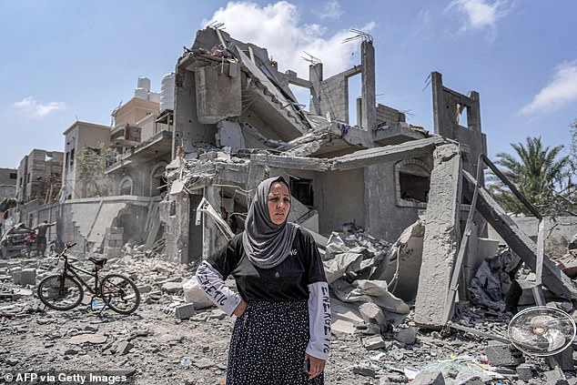 A woman stands among the rubble in front of a collapsed building on the eastern side of the Maghazi camp for Palestinian refugees in the central Gaza Strip