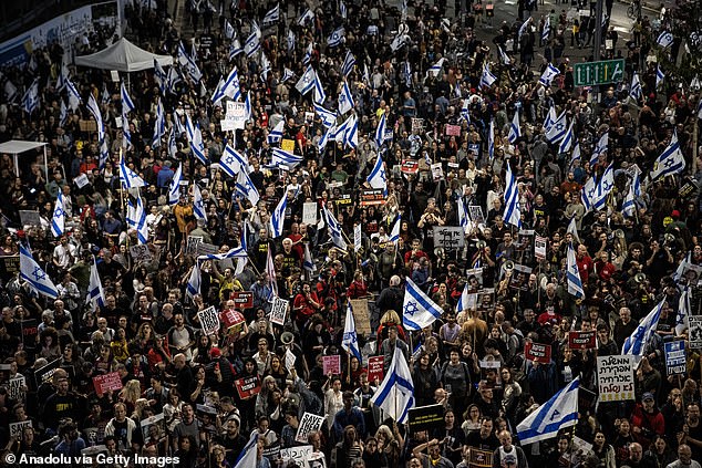 Netanyahu faces significant pressure at home from his citizens and within his own government.  (Image: Thousands carry Israeli flags and chant anti-government slogans as they protest Benjamin Netanyahu's resignation)