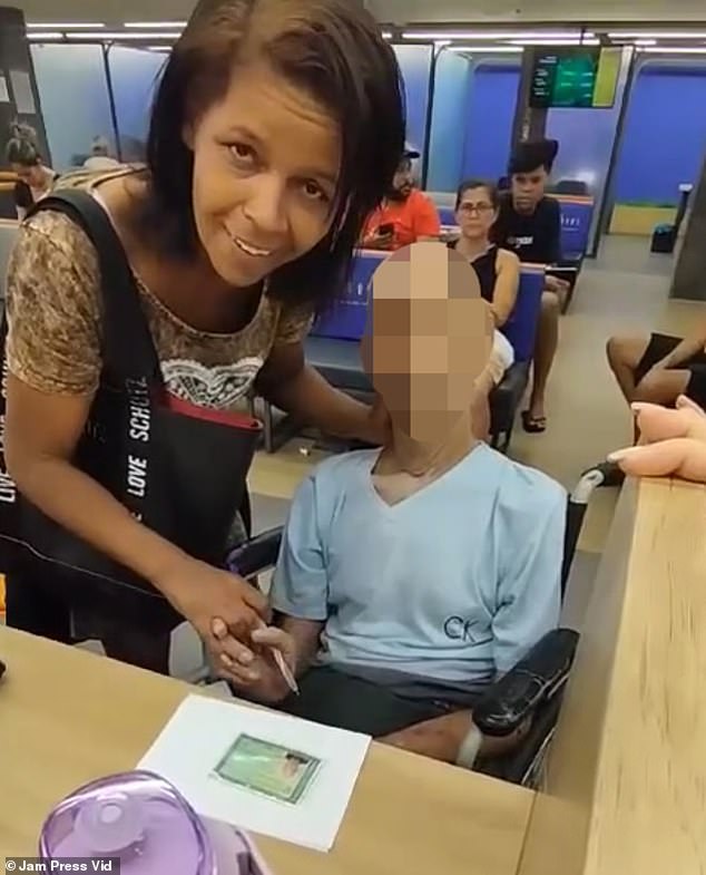 Érika de Souza holds Paulo Braga's hand and a pen while trying to get him to sign a loan document at a bank branch in Rio de Janeiro.  De Souza, a mother of six, said to her, “Uncle, are you listening?  You have to sign it.  I can't draw for you