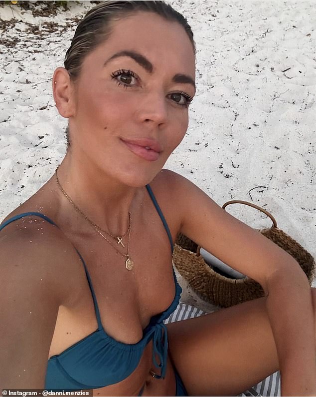 In a final solo selfie, Danni showed off her gold crucifix and pendant on the beach, sitting on a striped beach towel, with her straw bag in the background