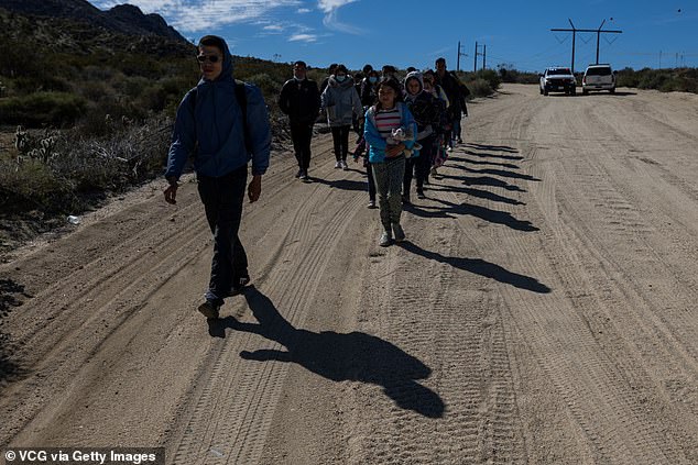 Migrants walk along a dirt road after crossing the nearby border with Mexico, near the Jacumba Hot Springs in San Diego, California