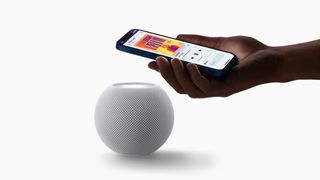 Someone holding an iPhone and playing Apple Music over an Apple HomePod smart speaker.