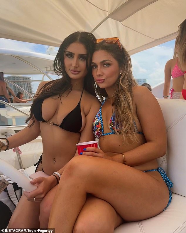 Two women in bikinis are seen posing on one of the many boats, while one has her hands on the wheel and the other holds a red solo cup