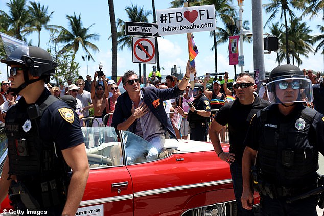The controversial Republican lawmaker was seen atop his red Chevy convertible as it rolled down Ocean Drive, holding up a sign saying he loves the Sunshine State