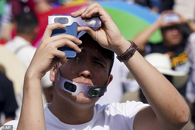 A man takes photos of a total solar eclipse in Mazatlan, Mexico, Monday, April 8, 2024. He uses eclipse glasses to protect his camera and eyes.