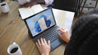 A woman sits at a table with a Windows laptop, opposite is a man who does not show his face