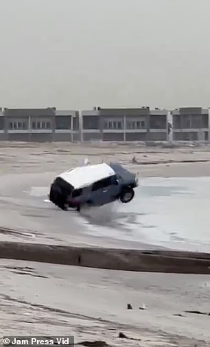 The car swerves before it appears to hit an edge and begins to roll on the sand