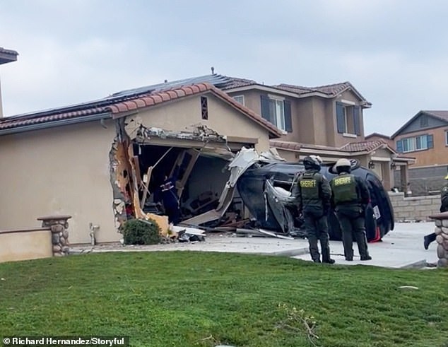 Police officers and firefighters assess the aftermath of the bizarre crash as the home's structure dangles and the car becomes stuck on its side