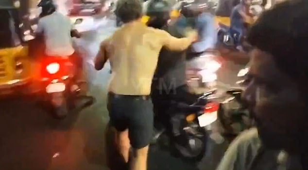 This is the moment a half-naked man launches himself at a passing motorcyclist before appearing to bite him