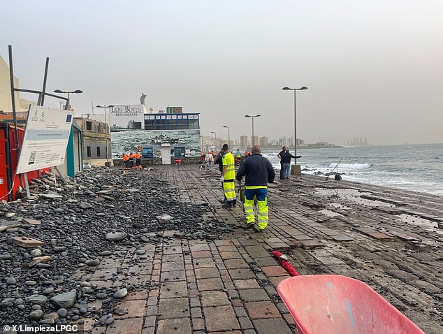 A tourist was killed and at least 130 people had to be evacuated as fierce storms hit Tenerife.  Pictured: Workers clearing up after the storm battered the Canary Island coast