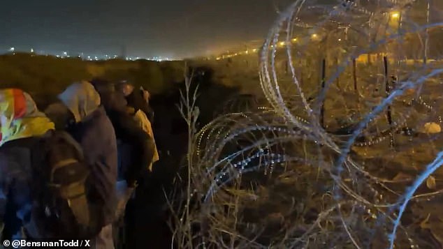 Migrants gather at the barbed wire fence between Mexico and a border crossing near El Paso, Texas, as Texas police and National Guard stand guard on the other side