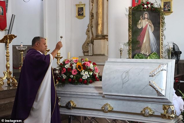 A priest at St. Peter the Apostle Cathedral sprinkles holy water over Wilevis Brito's coffin on Wednesday