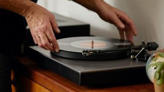 Cambridge Audio Alva TT V2 on sideboard, with man putting a record on the turntable