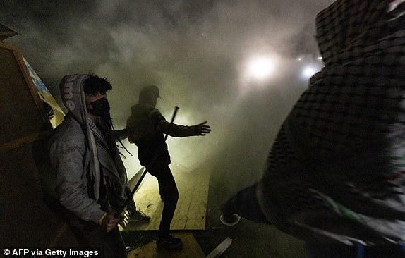 Pro-Palestinian protesters engulfed by tear gas regroup and rebuild the barricade around the encampment set up on the University of California Los Angeles (UCLA) campus when clashes with counter-protesters broke out in Los Angeles on May 1, 2024.  Clashes broke out.  on May 1, 2024 around pro-Palestinian demonstrations at the University of California, Los Angeles, as universities across the United States struggle to contain similar protests on dozens of campuses.  (Photo by ETIENNE LAURENT / AFP) (Photo by ETIENNE LAURENT/AFP via Getty Images)