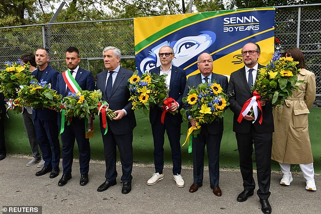 The foreign ministers of Brazil, Austria and Italy pose next to Domenicalli in front of a banner with flowers, right at the point of the crash that killed Senna