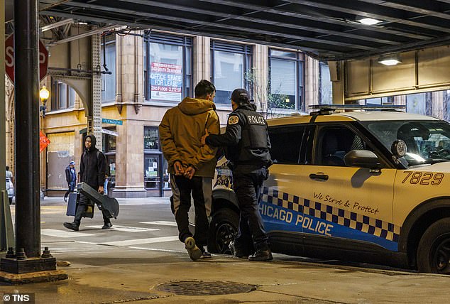 A Chicago police officer detains a migrant near a shelter at the former Standard Club in Chicago on April 16, 2024