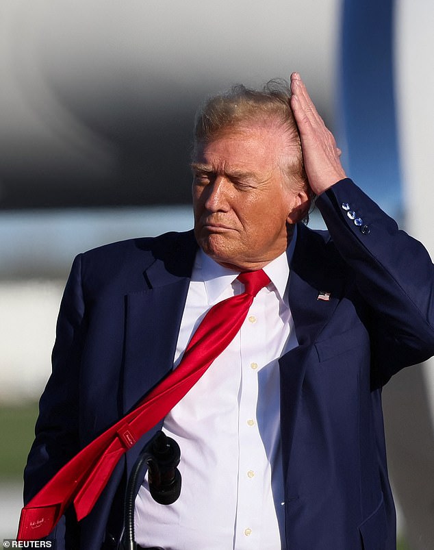 Trump tries to comb his hair back during a windy campaign event in Freeland.  MI.  Trump was visiting the 'pivot county' that he lost to Biden by just over 300 votes in 2020, but won in 2016