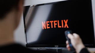 A man looks at the Netflix logo on a Toshiba TV with a remote control in his hand