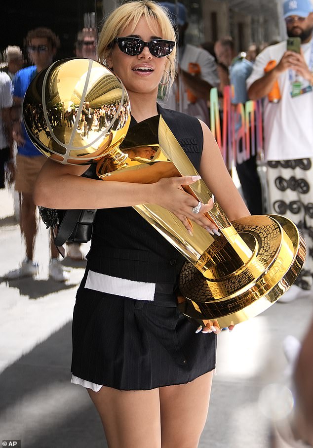 Camila Cabello holds the Larry O'Brien NBA Championship trophy in black and white dress