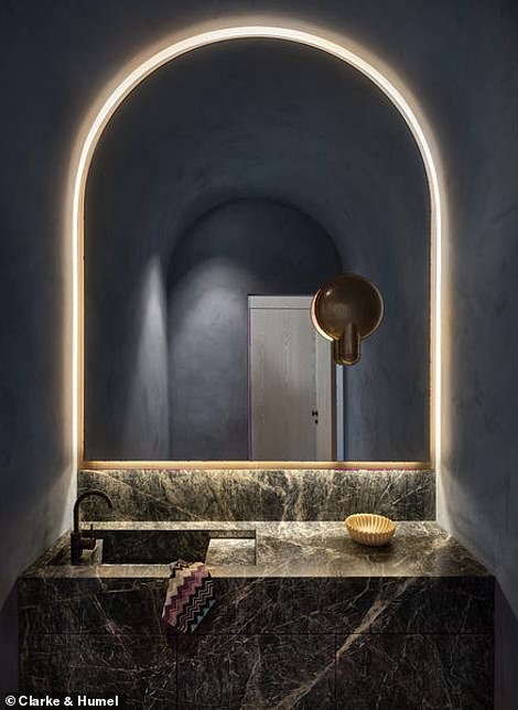 A vaulted powder room is fully decorated in a moody navy blue, while a black marble vanity and custom-lit curved mirror make guests feel like they are in a luxury hotel