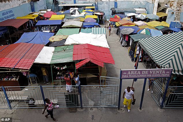 People walk in an open-air market where the government allows licensed vendors to sell their goods in Havana.  The entrance sign says 'Sales area for self-employed persons' in Spanish