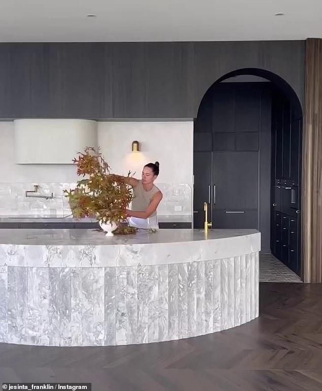 Jesinta shared a video of her setting up a floral display in the stone kitchen, which features a curved island bench, all-black cabinetry and a butler's pantry