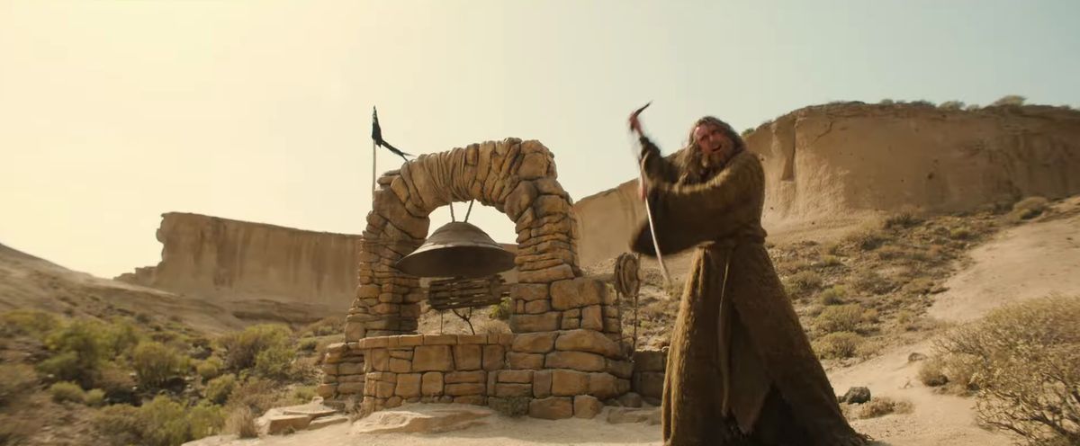 The Stranger brandishes his staff in a desert setting, with some sort of bell or spring behind him in the trailer for Season 2 of The Lord of the Rings: The Rings of Power