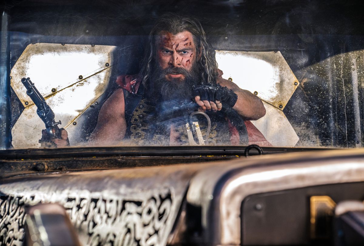 Dementus (Chris Hemsworth), a Wasteland warrior with shaggy hair and beard, holds a gun in one hand and drives a vehicle with the other in George Miller's Furiosa