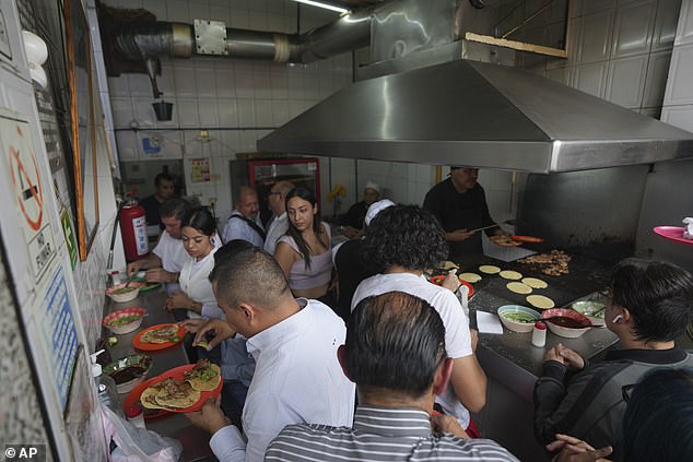 An overhead view of the small taco stand.  Customers line the side wall putting salsa on their tacos while the Michelin-starred chef continues to serve food