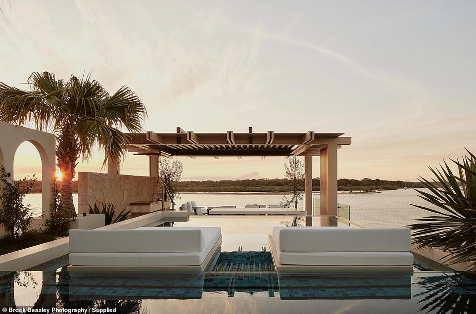 Two daybeds appear as if they are floating in the center of the blue-tiled, glass-edged pool, while Mediterranean-style arches give the space a Tuscan feel