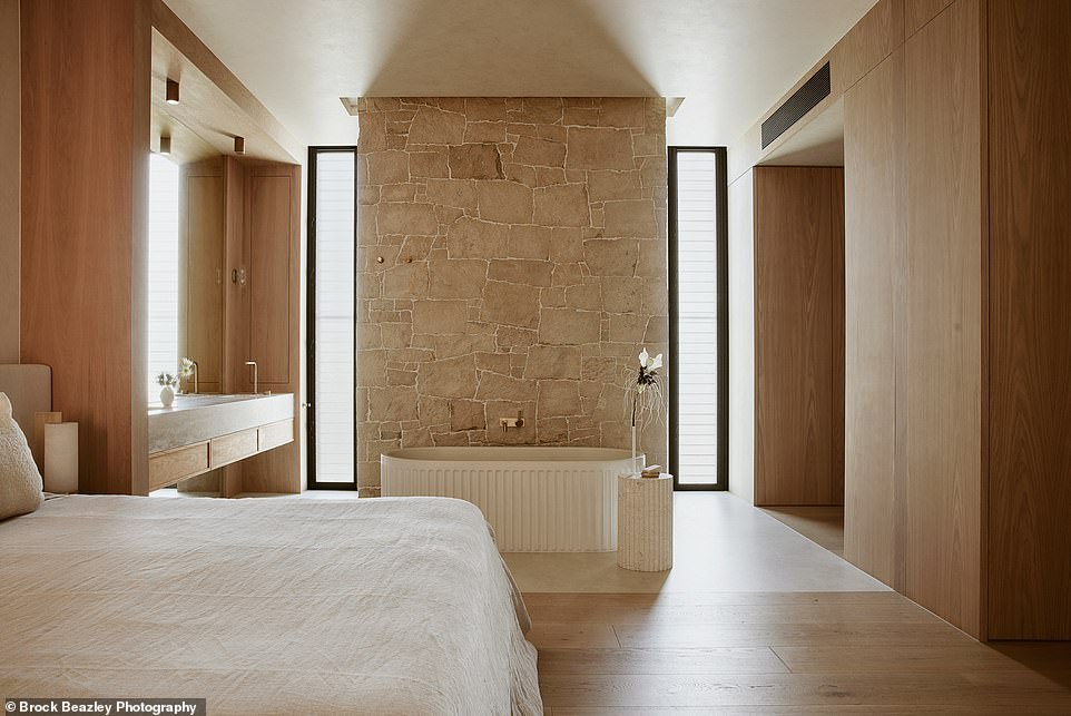 The opulent master bedroom has an open-plan bathroom with a freestanding, ribbed bath with a rustic stone wall and a hidden curved shower corner decorated with Japanese finger tiles.