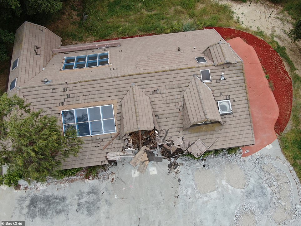 Roof shingles are missing and falling off, while green plants and trees are seemingly overgrown at the front of the main house